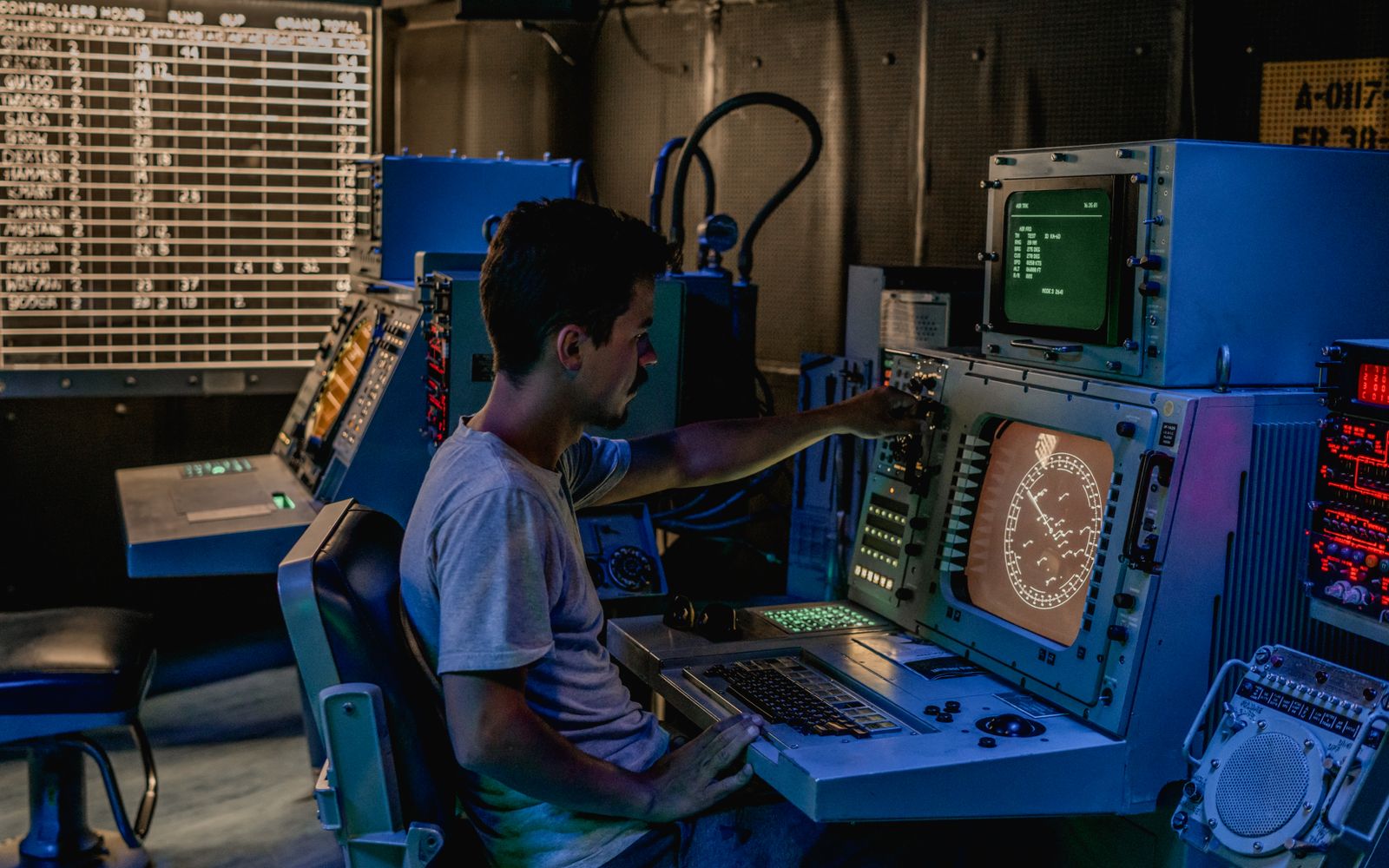 A man working at control panels in a dimly lit industrial room with various monitors.