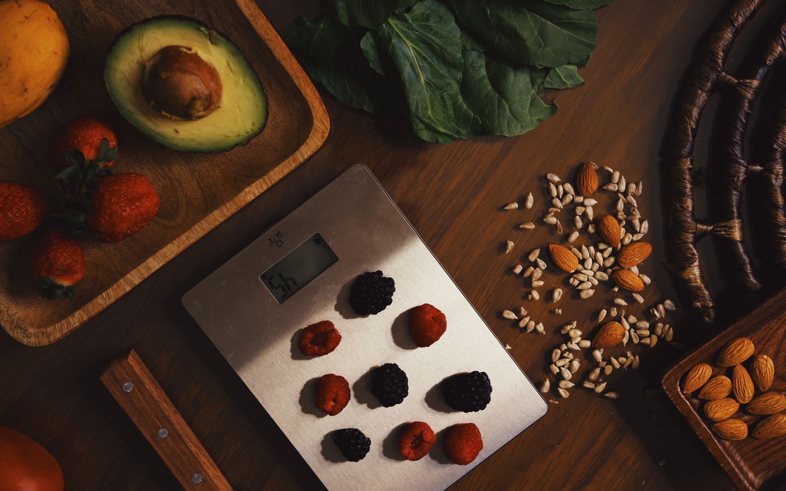 Top view of composed raw almond with seeds and avocado on table with berries on scales for cooking healthy dish
