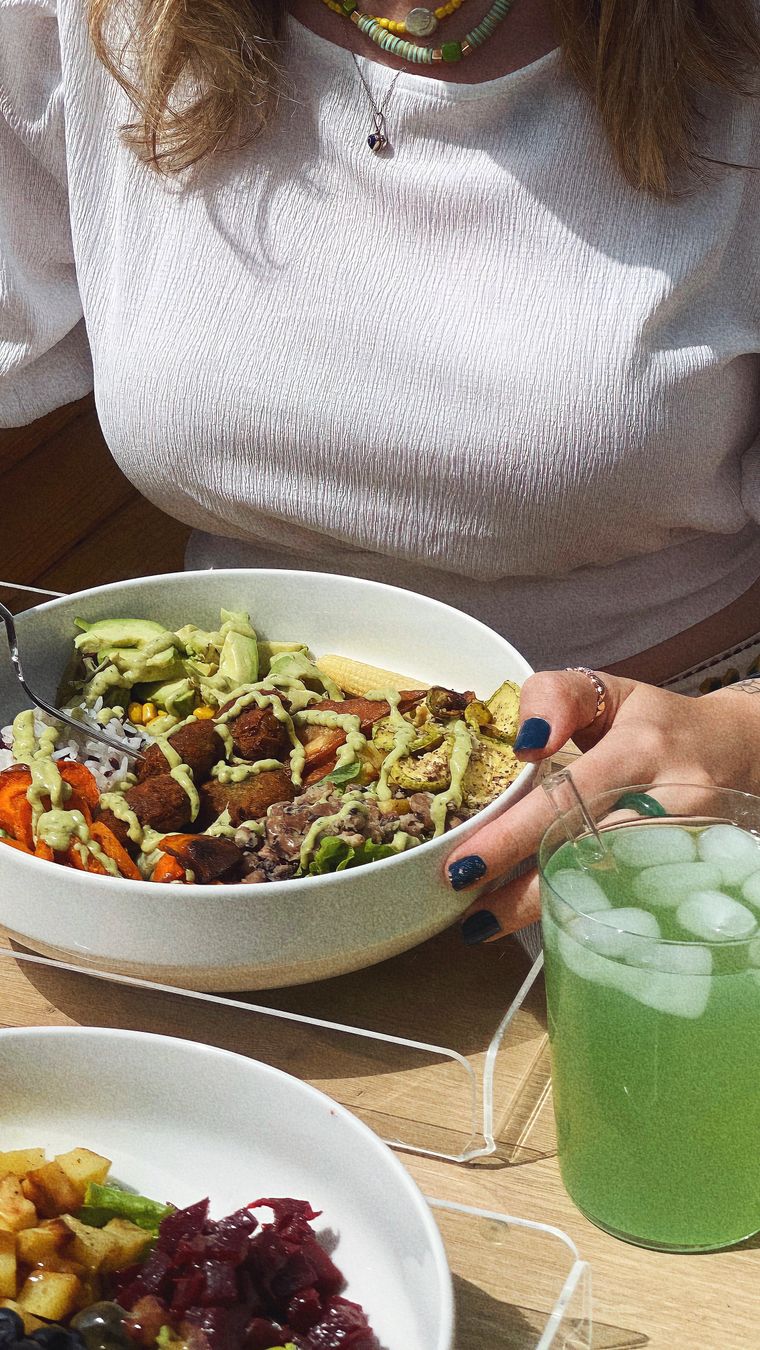 Woman savoring a nutritious avocado salad with a refreshing green drink on a sunny day.