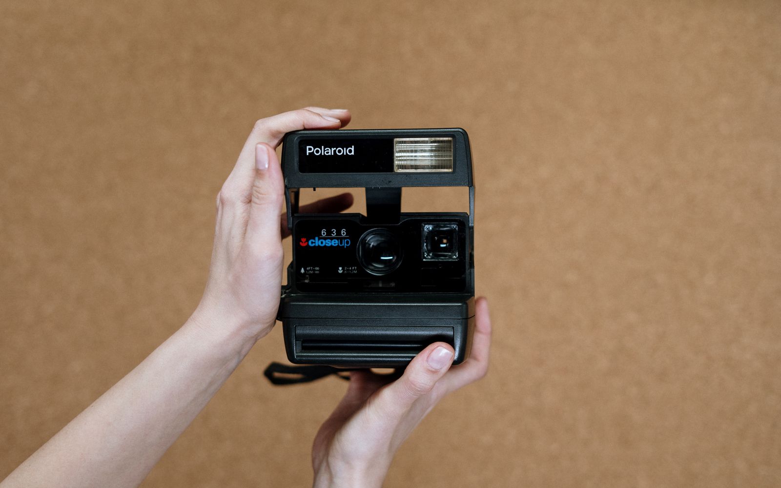 A person holds a classic Polaroid instant camera against a corkboard background, highlighting retro photographic equipment.