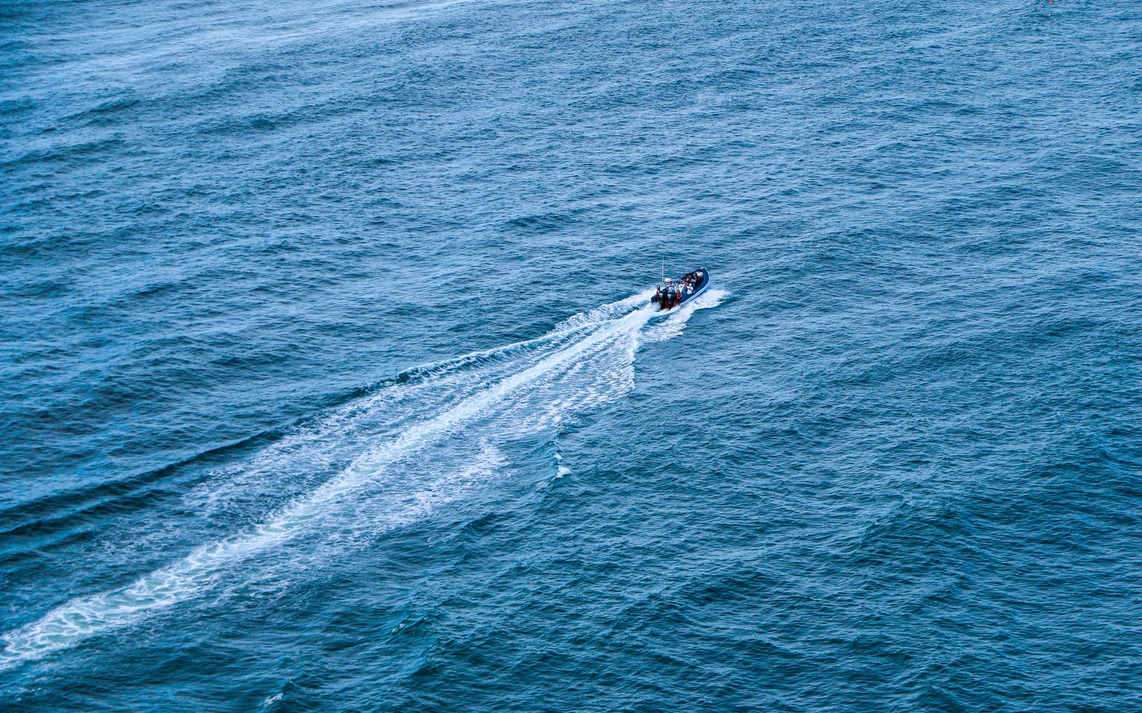 High-angle view of a speedboat slicing through turquoise ocean waters, creating white trails.