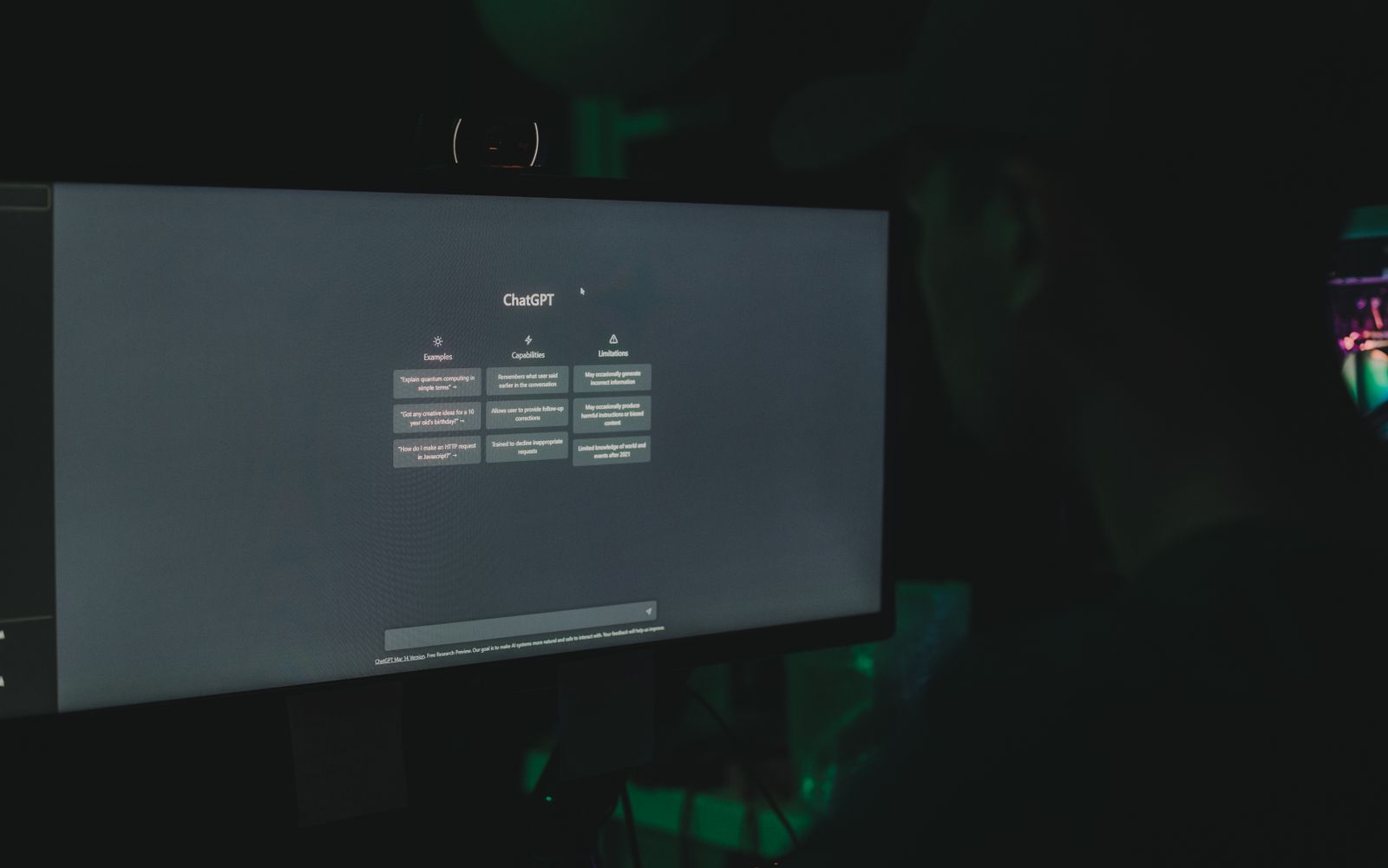 A person interacting with ChatGPT interface on a computer screen in a dimly lit room.