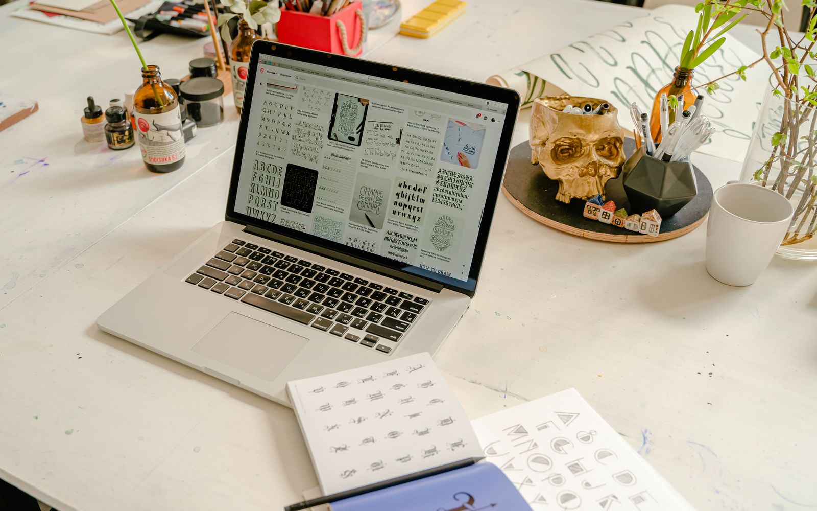 A creative workspace featuring a laptop, calligraphy book, and writing materials on a table.